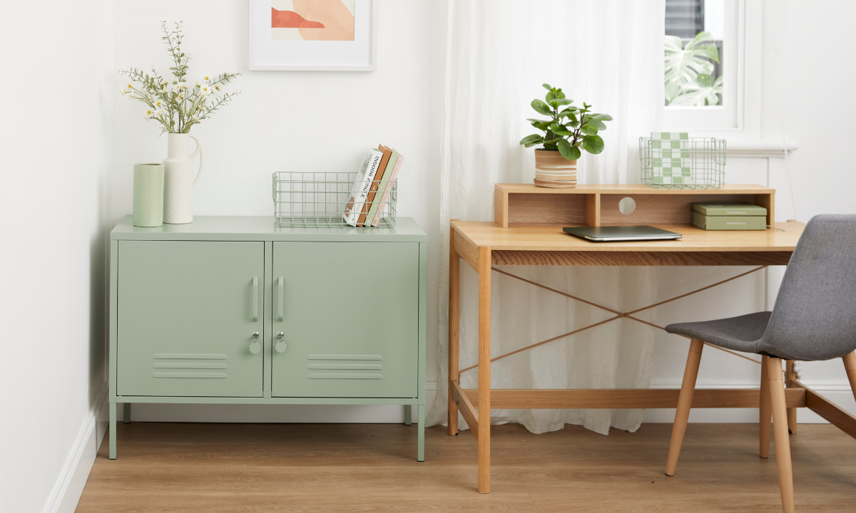 A Sage Lowdown locker sits in a home office next to a wooden desk with a chair. There is a laptop on the desk and small potted plants and books decorating the space.