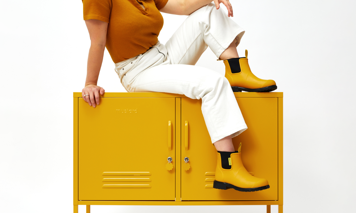 Becca sitting on top of The Lowdown Locker in Mustard, wearing Merry People boots.