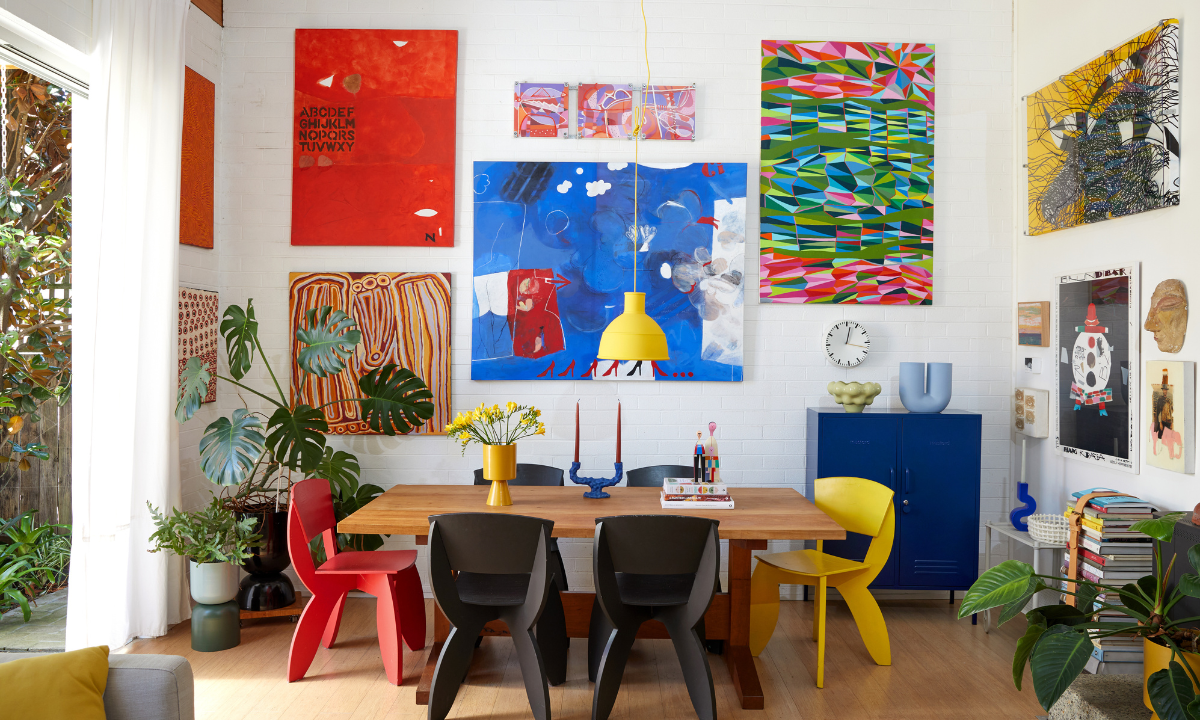 A colourful dining room featuring white brick walls, large abstract paintings and quirky chairs in red, black and yellow.