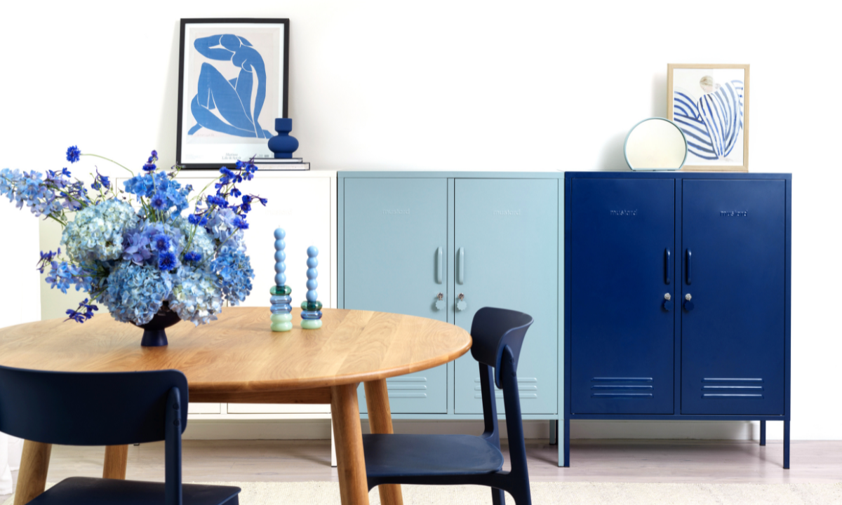 A trio of Midi lockers in an ombre pattern from white to Ocean to Navy are styled behind a round wooden dining table. There is a vase of luscious, full blue flowers and a selection of blue-toned artworks.