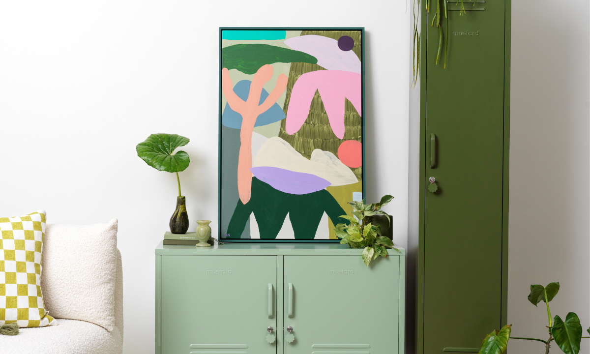 A brightly coloured print sits on top of a Sage Lowdown locker in a room filled with plants.