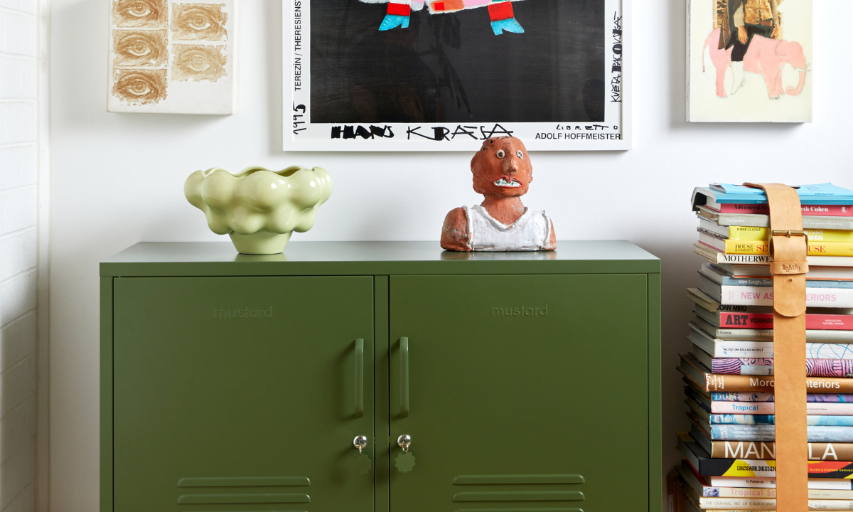 An Olive Lowdown Mustard Made Locker is styled next to a stack of coffee table books and an eclectic range of colourful artworks.