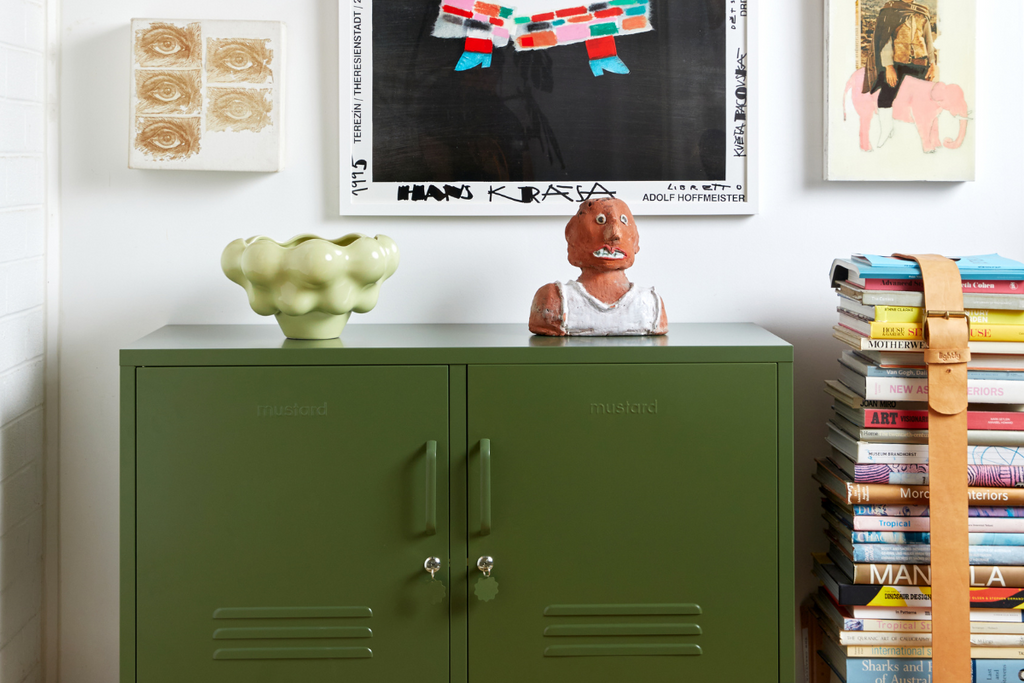 An Olive Lowdown Mustard Made Locker is styled next to a stack of coffee table books and an eclectic range of colourful artworks.