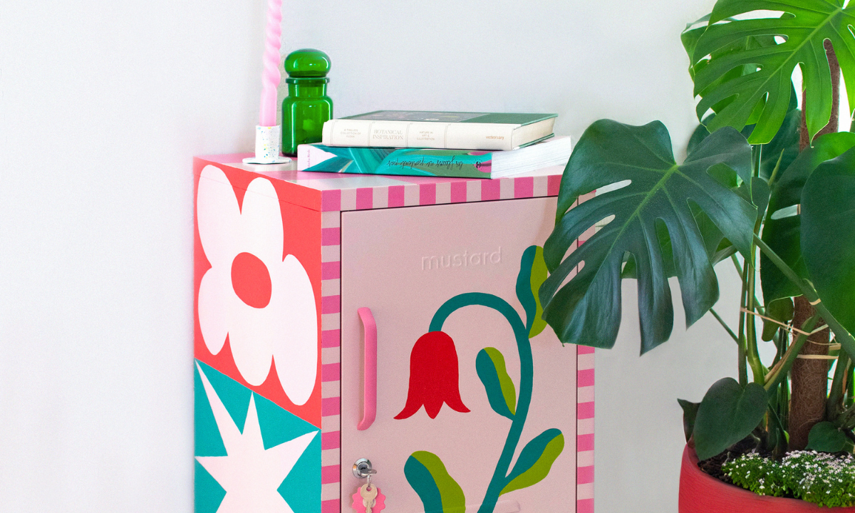 A Blush Shorty has been painted with a detailed floral design, with the edges in a pink checkerboard pattern. There is a monstera plant in a red pot beside it.