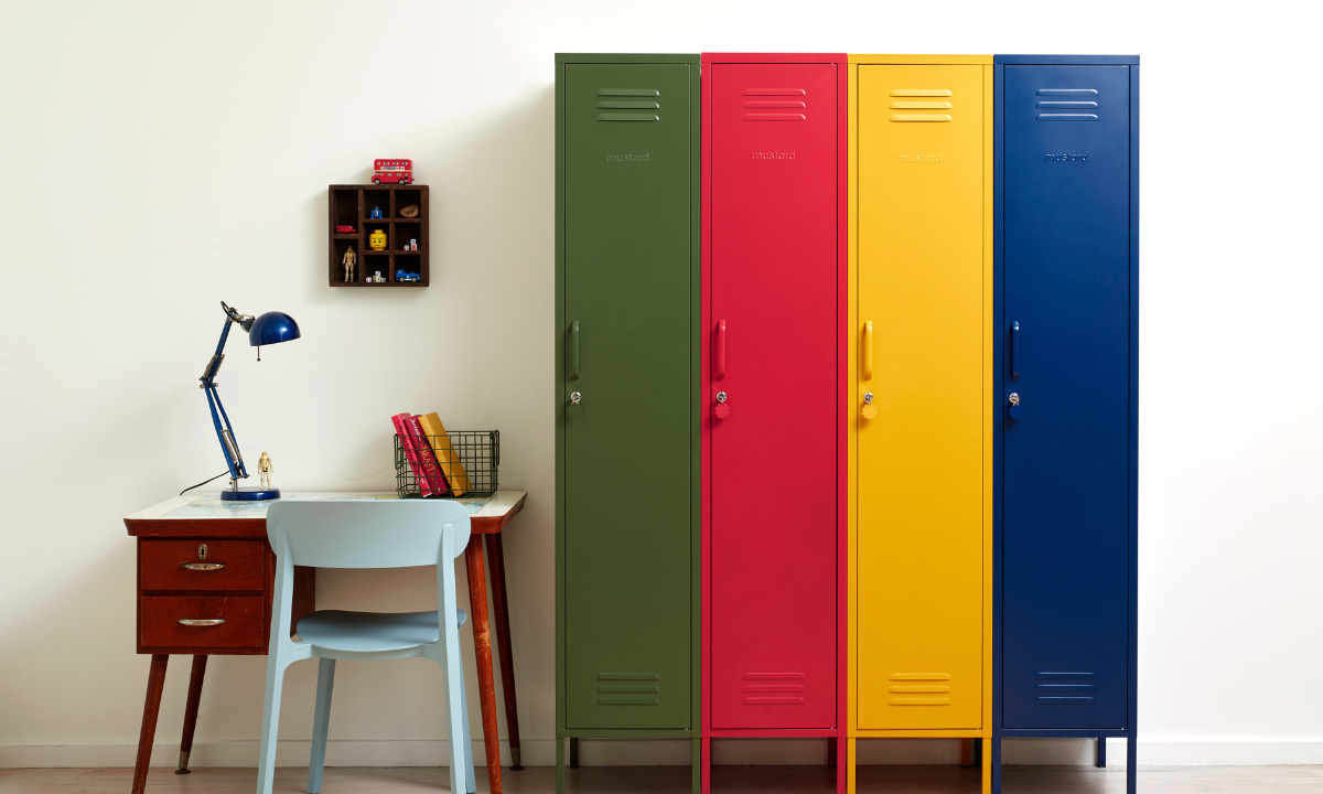 Four brightly coloured Skinny lockers sit side by side to create a rainbow of primary colours. Next to them is a small wooden desk with a pale blue chair.