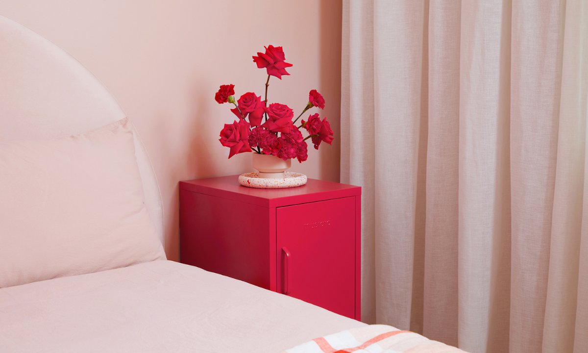 The Shorty in Poppy next to a bed, with a vase of red roses on top