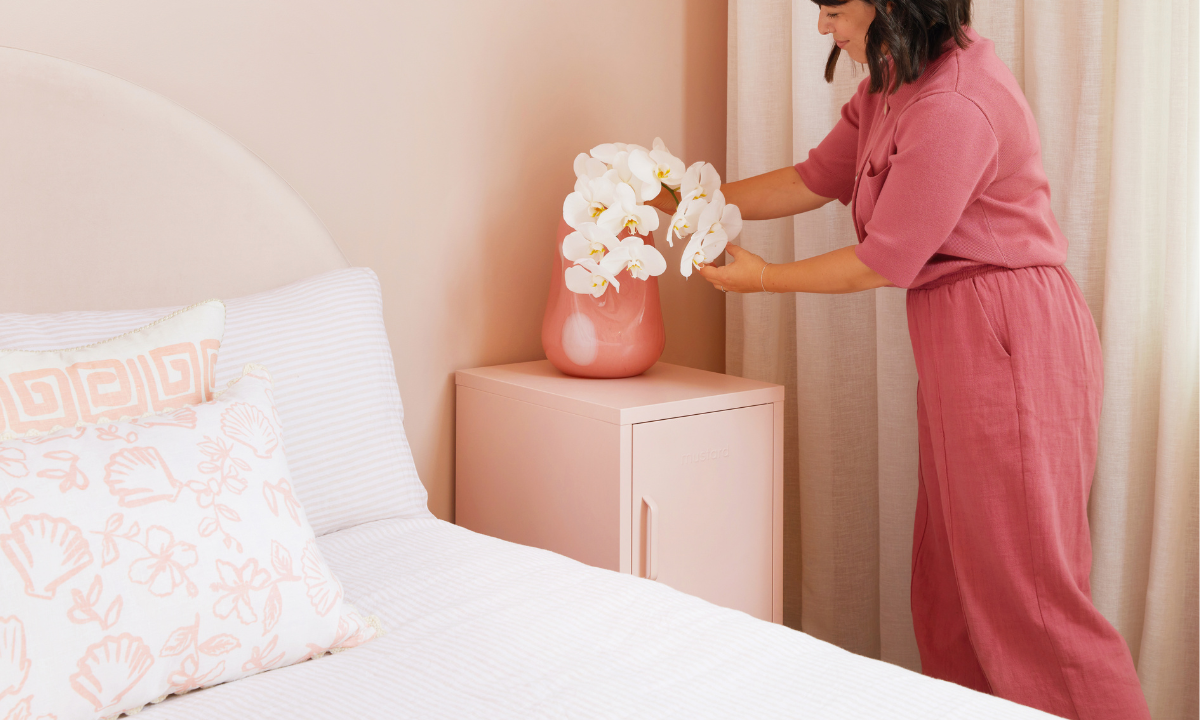 Becca is wearing a Berry coloured outfit and arranging some flowers in a vase on top of a Blush Shorty. The whole room is styled in Blush tones.